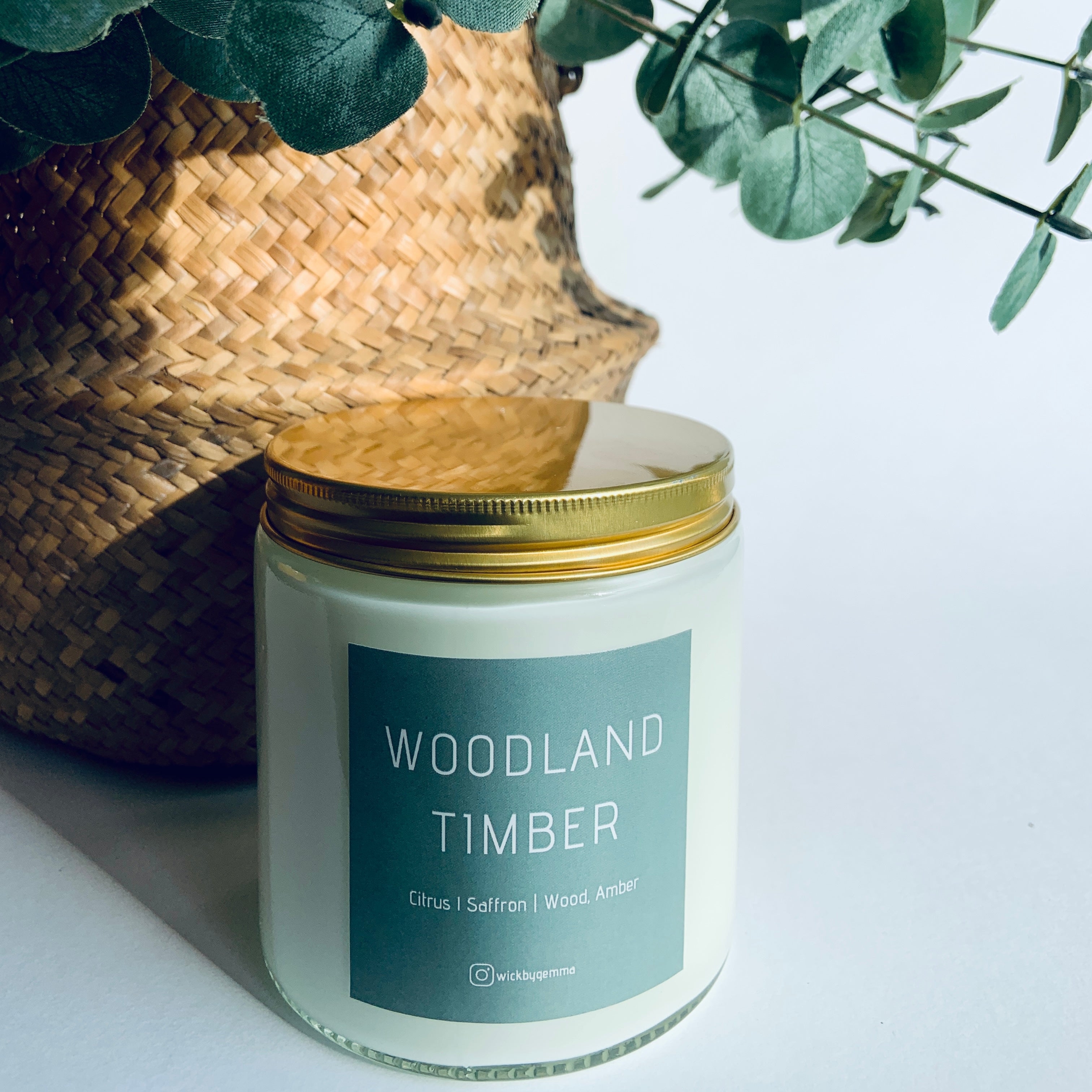 Candle labeled 'Woodland Timber' with a plant in the background