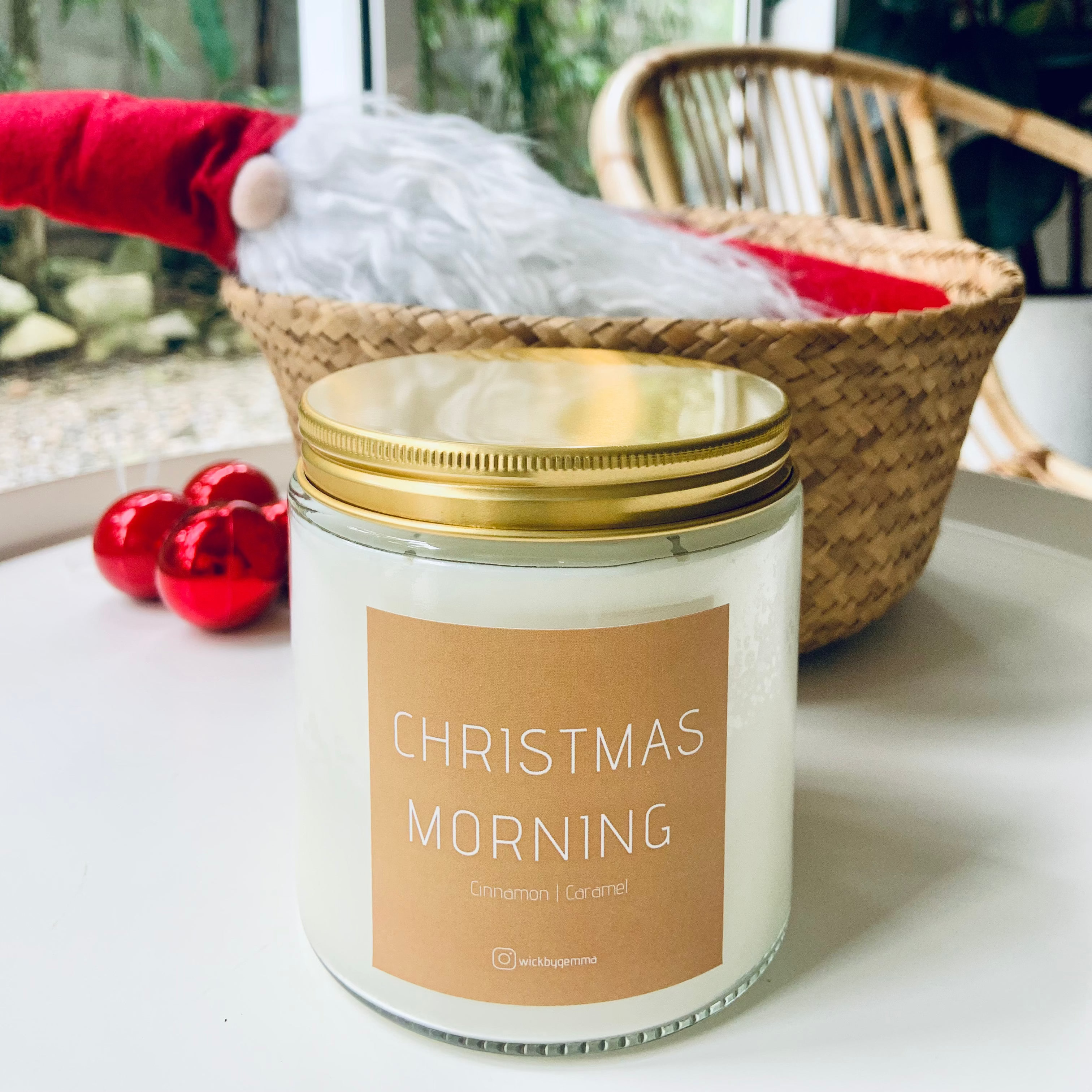Candle labeled 'Christmas Morning' on a table with a window and plant in the background