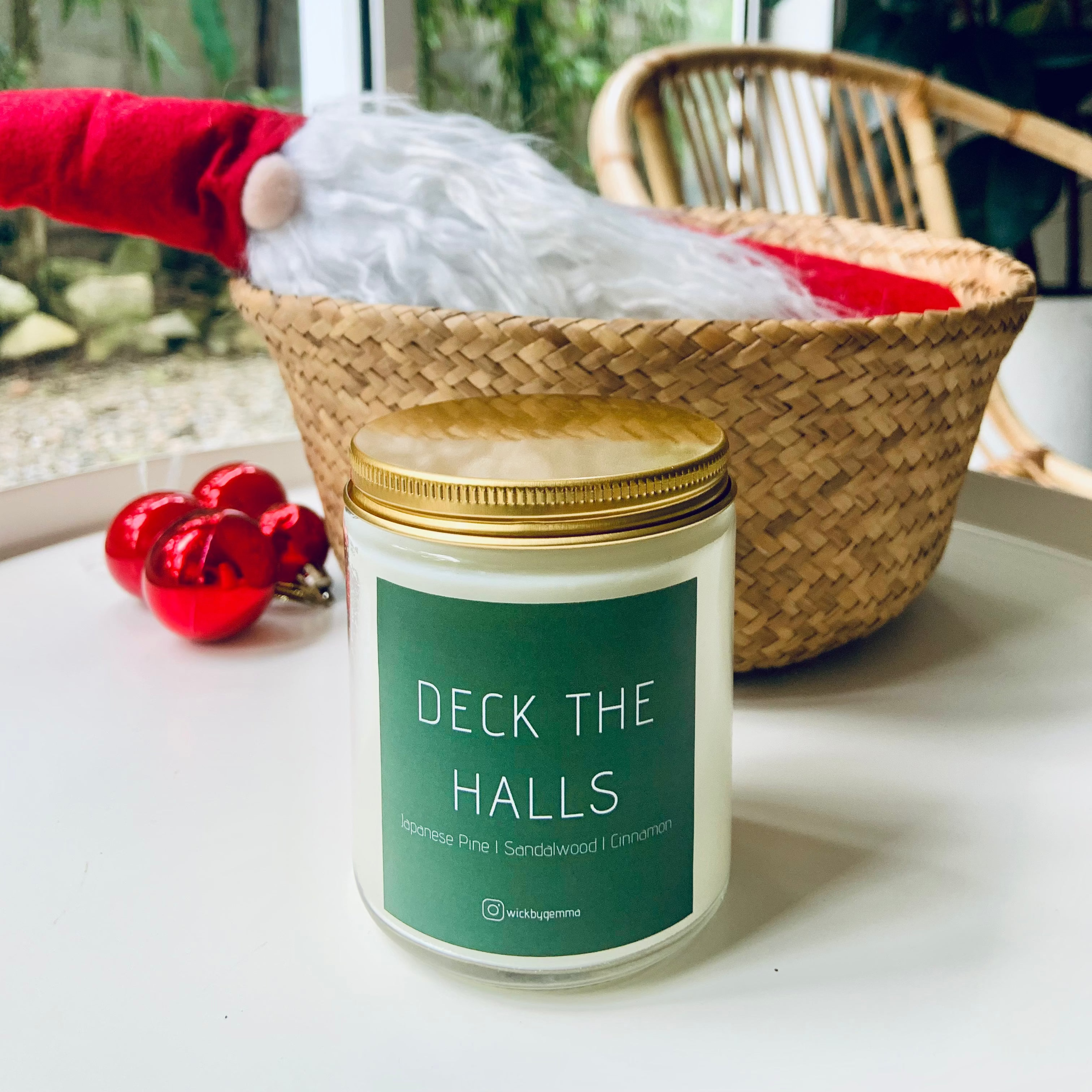 Candle labeled 'Deck the Halls' on a surface with a decorative basket and gnome in the background.