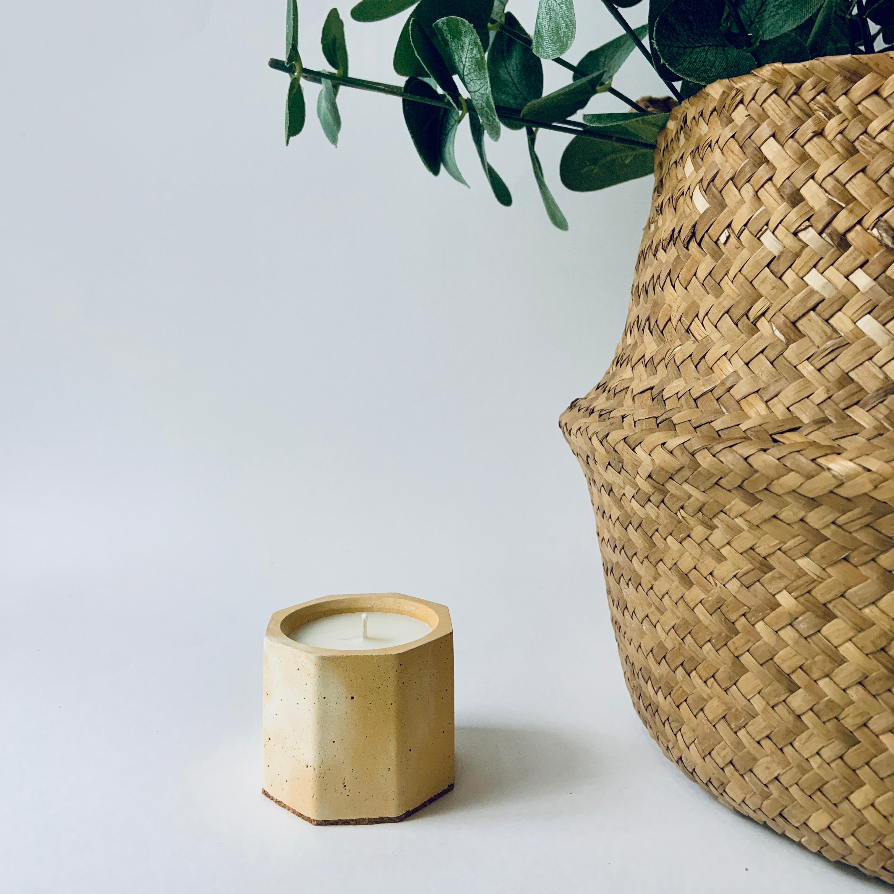 Bamboo candle holder with a lit candle next to a woven basket on a light background