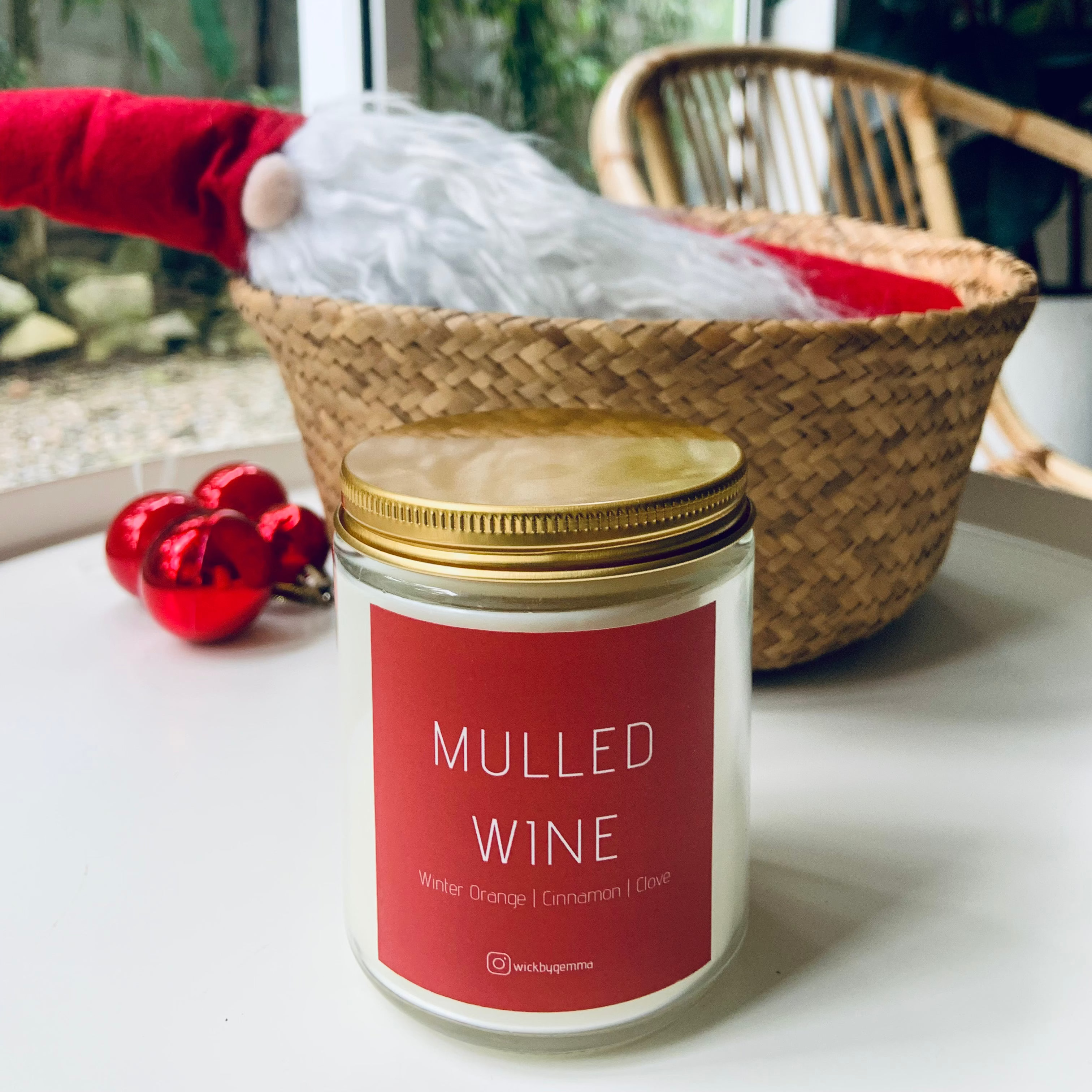 Candle labeled 'Mulled Wine' on a surface with a window and basket in the background