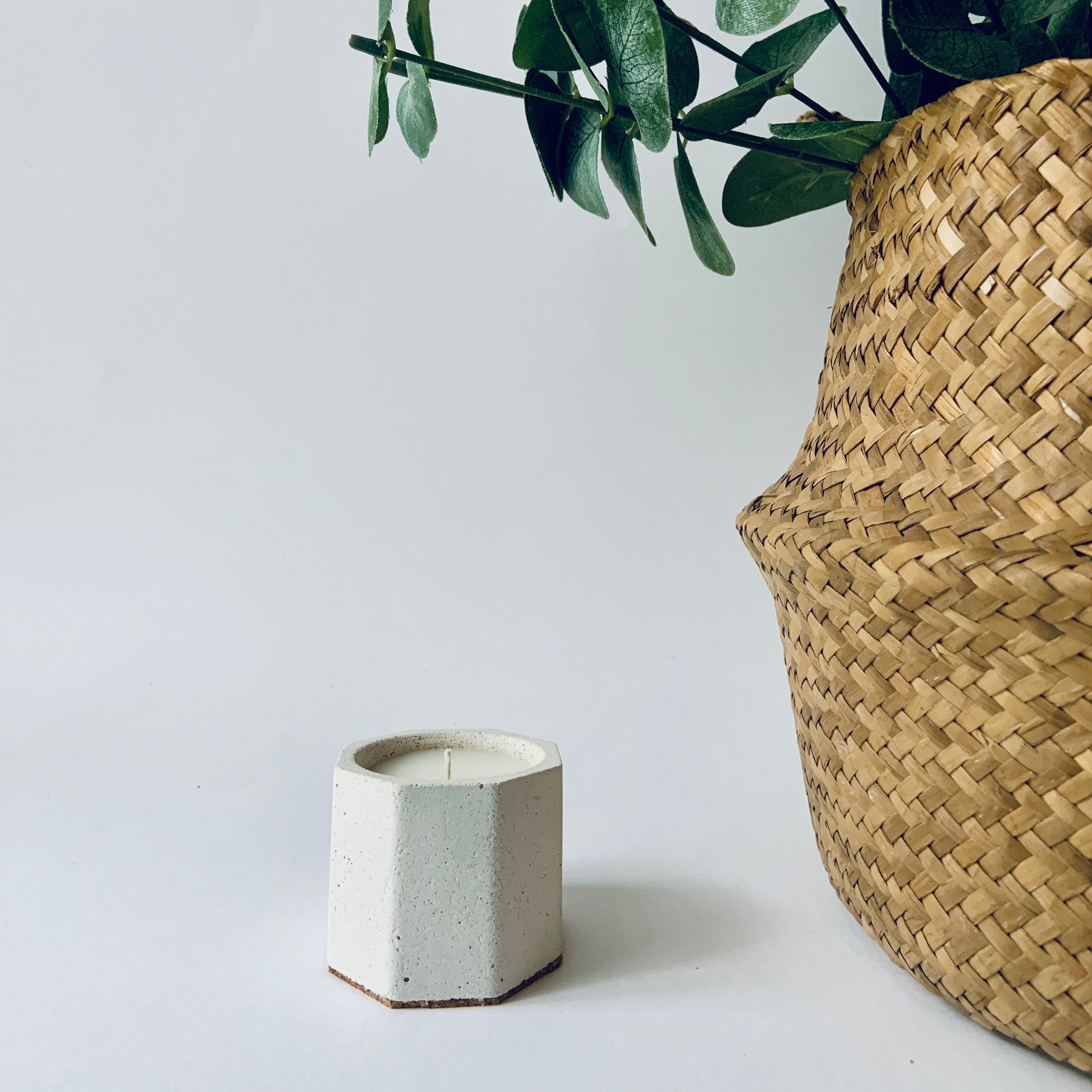 Hexagonal concrete candle holder with a woven basket and plant on a light background